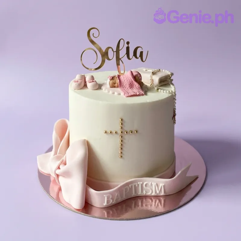 A white 1-tier Baptism cake, featuring a sleeping baby topper, gold 'Sofia' name, pink bow, and a gold beaded cross. A white 1-tier Baptism cake, featuring a sleeping baby topper, gold 'Sofia' name, pink bow, and a gold beaded cross.