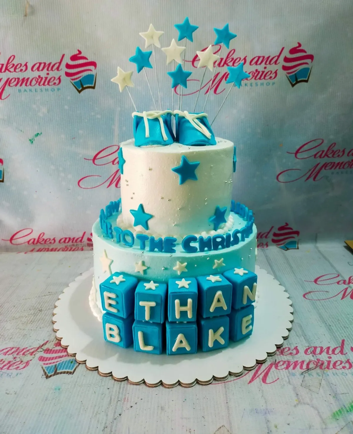 Two-tier blue and white baby boy baptism cake with fondant baby shoes, stars, and name blocks. Two-tier blue and white baby boy baptism cake with fondant baby shoes, stars, and name blocks.