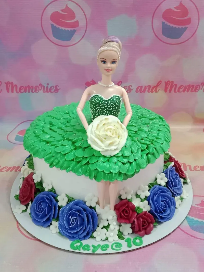 Barbie doll cake with a green ruffled icing dress and a white rose, surrounded by blue and red icing flowers on a white base. Barbie doll cake with a green ruffled icing dress and a white rose, surrounded by blue and red icing flowers on a white base.
