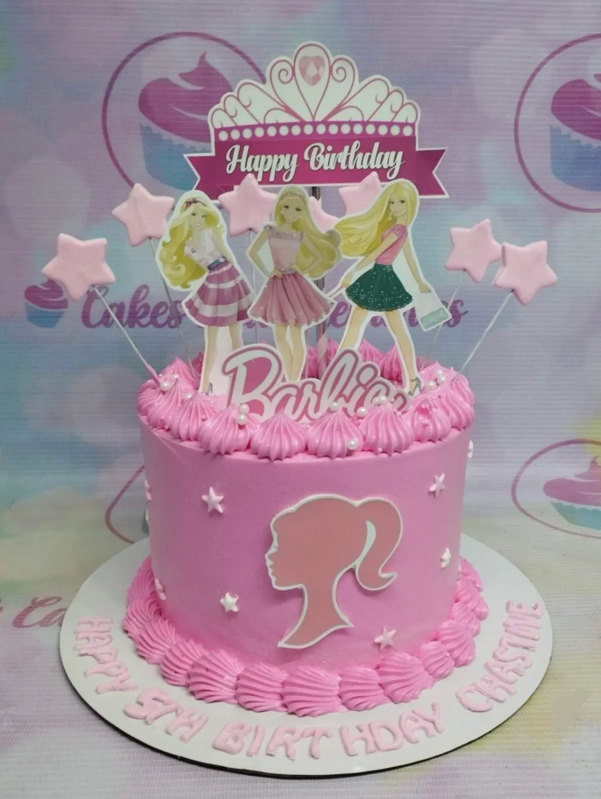 Pink Barbie themed birthday cake with character printouts, a crown topper, and pink icing swirls. Pink Barbie themed birthday cake with character printouts, a crown topper, and pink icing swirls.