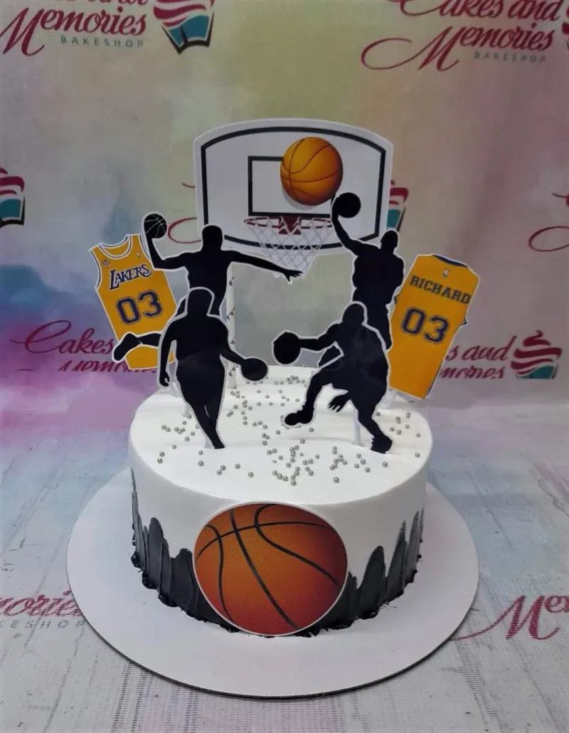 Basketball themed birthday cake with black player silhouettes, Lakers jersey printouts, and a basketball hoop topper on white icing. Basketball themed birthday cake with black player silhouettes, Lakers jersey printouts, and a basketball hoop topper on white icing.