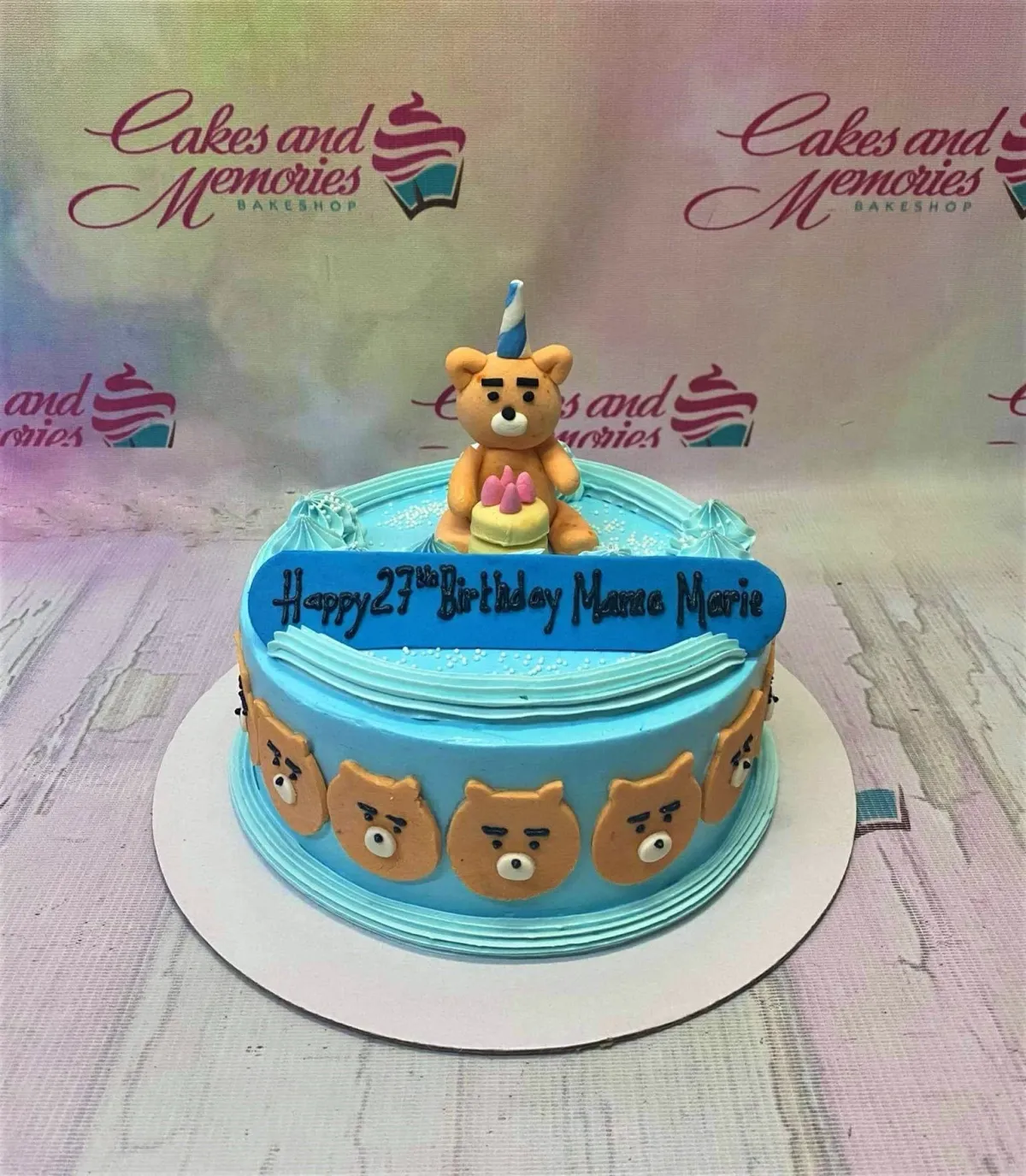 Light blue birthday cake featuring a 3D fondant bear topper with a party hat and multiple bear face decorations on the side. Light blue birthday cake featuring a 3D fondant bear topper with a party hat and multiple bear face decorations on the side.