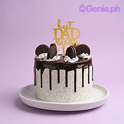 A single-tier white cake with black cookie crumbs, chocolate drip, whipped cream dollops, Oreo cookies, and a gold Best Dad Ever topper. A single-tier white cake with black cookie crumbs, chocolate drip, whipped cream dollops, Oreo cookies, and a gold Best Dad Ever topper.