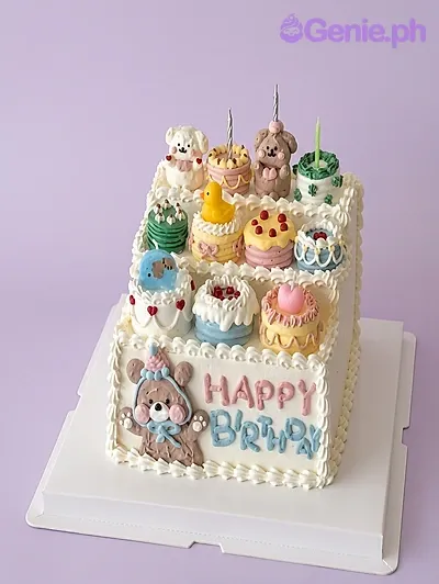 Square white cake with bears, a yellow duck, and various mini cakes Square white cake with bears, a yellow duck, and various mini cakes