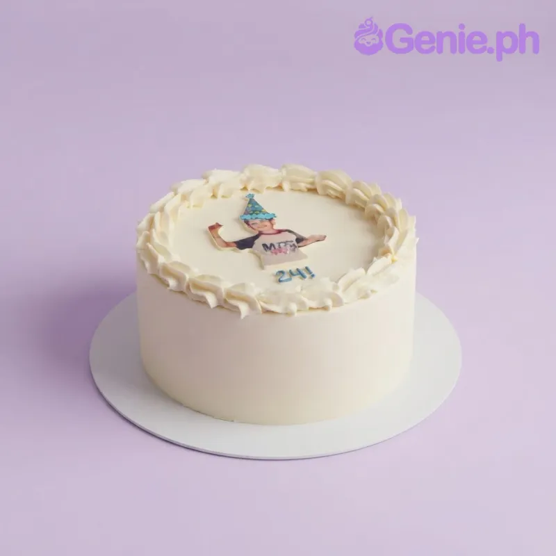 White 1-tier cake with soft icing, a piped border, a photo printout of a person in a party hat, and blue piped age text White 1-tier cake with soft icing, a piped border, a photo printout of a person in a party hat, and blue piped age text