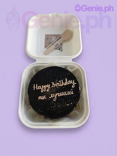 A black and gold bento cake themed for a birthday, featuring gold glitter, gold icing text, and presented with wooden cutlery. A black and gold bento cake themed for a birthday, featuring gold glitter, gold icing text, and presented with wooden cutlery.