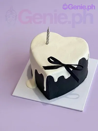 A black and white heart-shaped 1-tier cake themed around minimalism, featuring a silver candle, white icing drip, and a black ribbon bow. A black and white heart-shaped 1-tier cake themed around minimalism, featuring a silver candle, white icing drip, and a black ribbon bow.