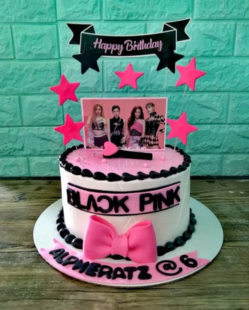Blackpink themed birthday cake with pink and white icing, black borders, a large pink bow, and printed character toppers. Blackpink themed birthday cake with pink and white icing, black borders, a large pink bow, and printed character toppers.