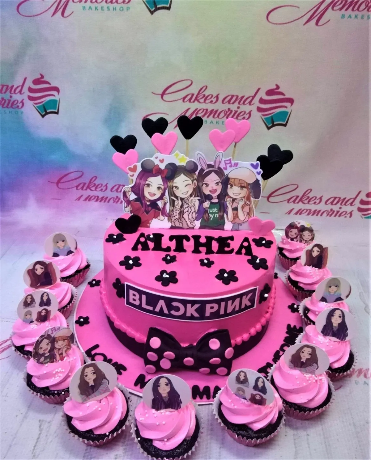 Pink Blackpink themed birthday cake for Althea with character printouts, a black bow, and matching cupcakes. Pink Blackpink themed birthday cake for Althea with character printouts, a black bow, and matching cupcakes.