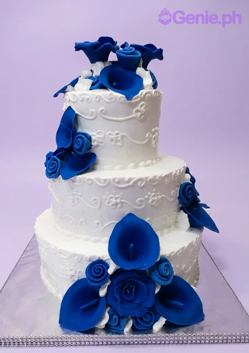 A white and blue 3-tier cake themed as Blue Floral Wedding, featuring blue gumpaste flowers and white icing scrollwork. A white and blue 3-tier cake themed as Blue Floral Wedding, featuring blue gumpaste flowers and white icing scrollwork.