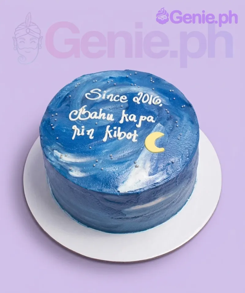 A blue, white, and silver 1-tier cake themed as a Blue Galaxy, featuring a yellow crescent moon, silver dragees, and white icing text. A blue, white, and silver 1-tier cake themed as a Blue Galaxy, featuring a yellow crescent moon, silver dragees, and white icing text.