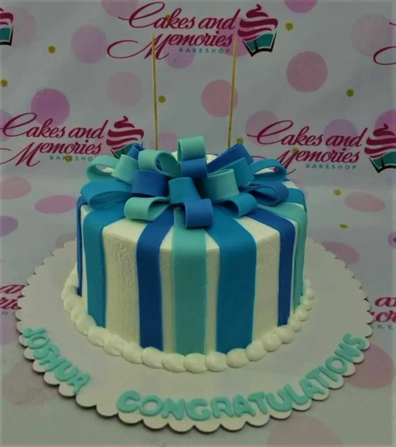A white round cake with blue and teal vertical fondant stripes and a large multi-colored fondant bow. A white round cake with blue and teal vertical fondant stripes and a large multi-colored fondant bow.