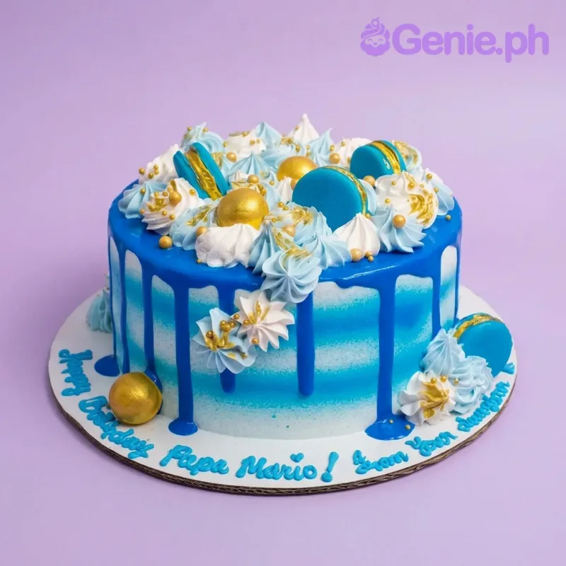 A blue and white 1-tier birthday cake featuring blue macarons, gold spheres, striped icing, and rosettes. A blue and white 1-tier birthday cake featuring blue macarons, gold spheres, striped icing, and rosettes.