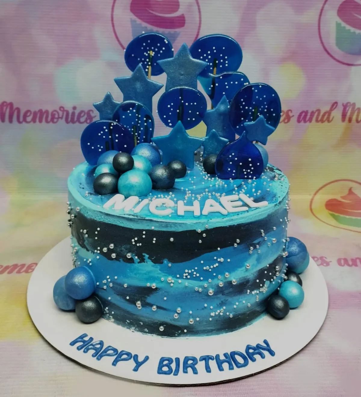 A blue and black 1-tier Blue Marble Galaxy cake, featuring blue stars, lollipops, spheres, and silver dragees. A blue and black 1-tier Blue Marble Galaxy cake, featuring blue stars, lollipops, spheres, and silver dragees.