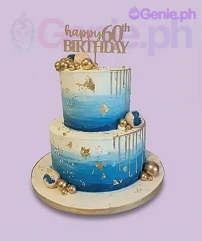 A blue, white, and gold two-tier 60th Birthday cake, featuring a gold 'Happy 60th Birthday' topper, gold drip, and gold spheres. A blue, white, and gold two-tier 60th Birthday cake, featuring a gold 'Happy 60th Birthday' topper, gold drip, and gold spheres.
