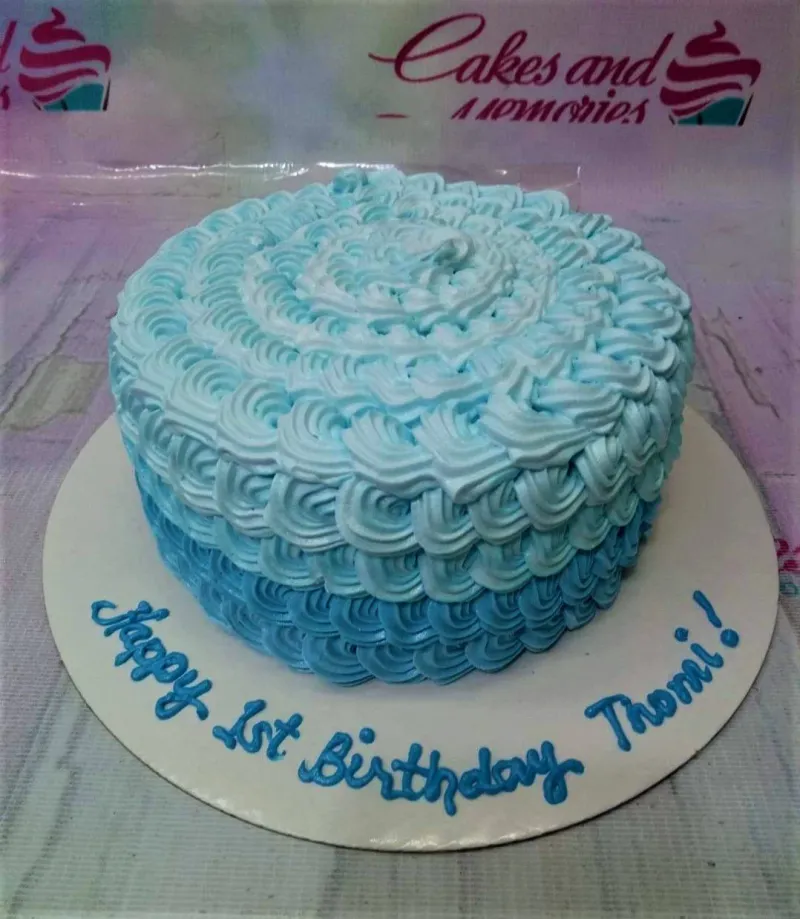 A blue ombre 1-Tier cake themed with rosettes, featuring all-over icing rosettes and a piped blue message on a white base board. A blue ombre 1-Tier cake themed with rosettes, featuring all-over icing rosettes and a piped blue message on a white base board.