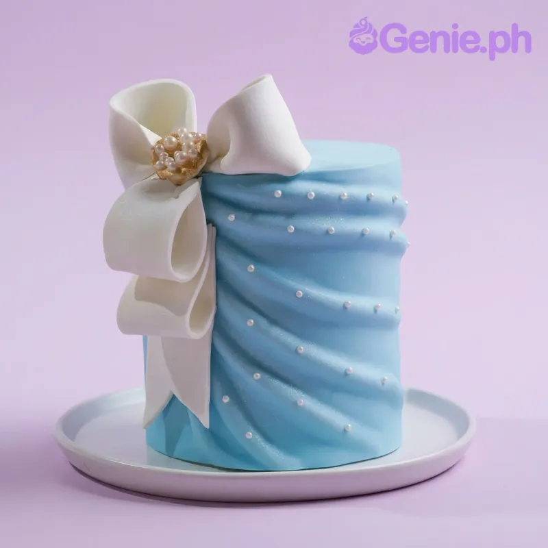 A light blue and white 1-Tier cake themed around a blue ribbon, featuring a large white gumpaste bow and white edible pearl accents. A light blue and white 1-Tier cake themed around a blue ribbon, featuring a large white gumpaste bow and white edible pearl accents.
