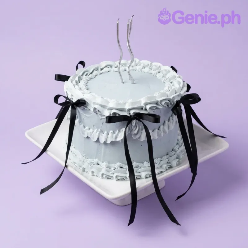 A light blue 1 Tier cake themed around vintage ribbon, featuring two silver taper candles and black bows with ruffled icing. A light blue 1 Tier cake themed around vintage ribbon, featuring two silver taper candles and black bows with ruffled icing.