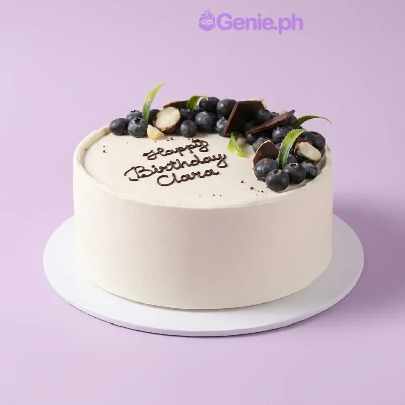 Blueberry Cake cake design — 1 layer soft icing cake in white — with chocolate pieces, blueberries, and custom "Happy" message Blueberry Cake cake design — 1 layer soft icing cake in white — with chocolate pieces, blueberries, and custom "Happy" message