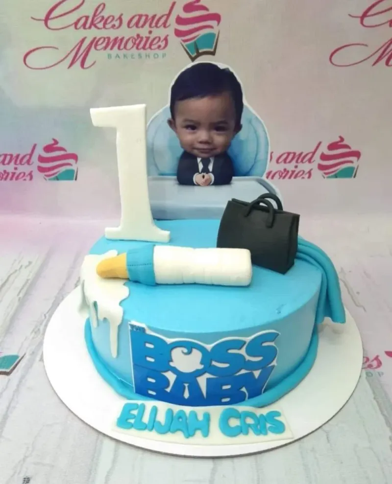 Light blue Boss Baby themed birthday cake with a photo printout of a baby, a fondant milk bottle, and a black briefcase topper. Light blue Boss Baby themed birthday cake with a photo printout of a baby, a fondant milk bottle, and a black briefcase topper.