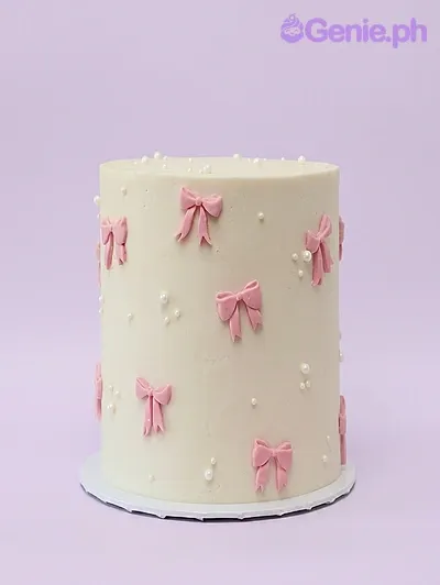 Ivory single-tier cake decorated with small pink fondant bows and white pearl dragees Ivory single-tier cake decorated with small pink fondant bows and white pearl dragees