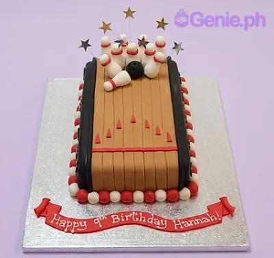 Bowling lane cake with fondant bowling pins, a black bowling ball, and a red banner message on a silver board. Bowling lane cake with fondant bowling pins, a black bowling ball, and a red banner message on a silver board.