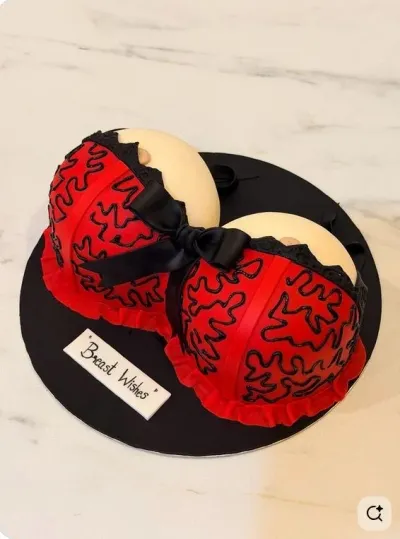 A breast-shaped 1-Tier Fondant cake with red lingerie, black lace, a black bow, and 'Breast Wishes' text. A breast-shaped 1-Tier Fondant cake with red lingerie, black lace, a black bow, and 'Breast Wishes' text.