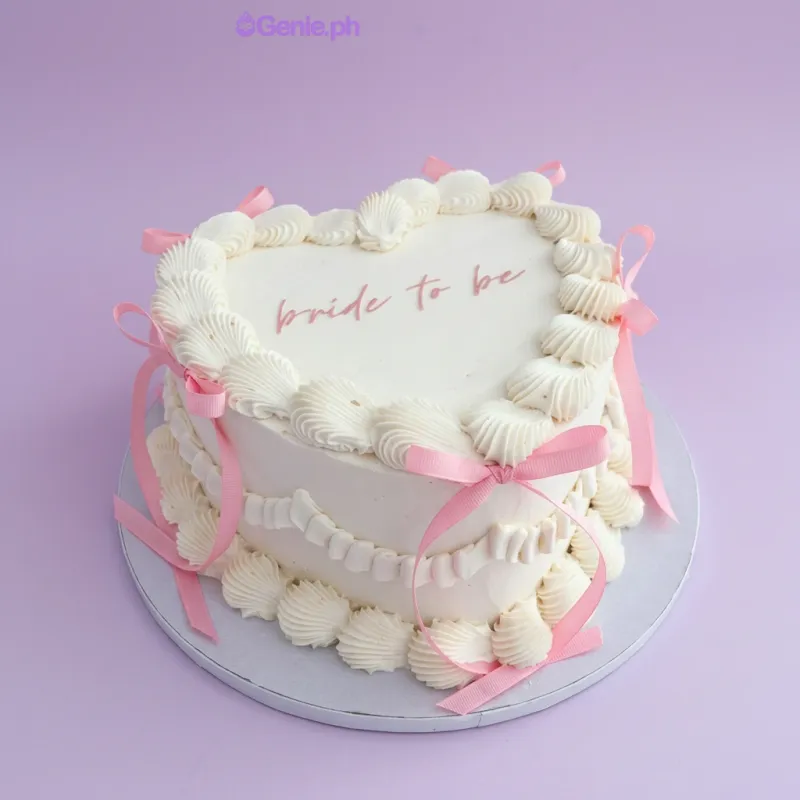 White heart-shaped cake with soft icing, piped shell borders, pink satin ribbons, and a bride to be message White heart-shaped cake with soft icing, piped shell borders, pink satin ribbons, and a bride to be message