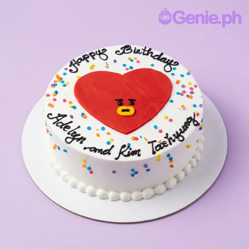 A white round 1-tier cake themed around BT21 Tata, featuring a large red heart character face, colorful confetti sprinkles, and black piped text. A white round 1-tier cake themed around BT21 Tata, featuring a large red heart character face, colorful confetti sprinkles, and black piped text.