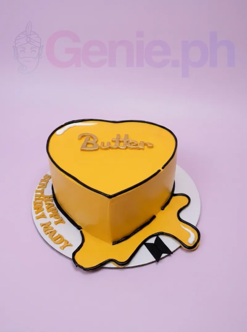 A yellow heart-shaped BTS Butter cake, with 'Butter' topper, BTS logo, outlines, and melting butter. A yellow heart-shaped BTS Butter cake, with 'Butter' topper, BTS logo, outlines, and melting butter.