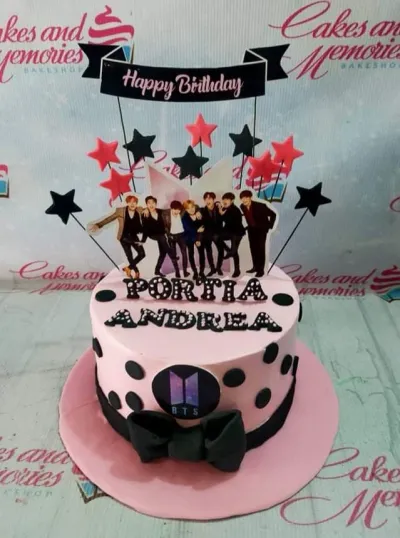 Pink BTS themed birthday cake with black polka dots, a large black bow, and printout toppers of the band members and stars. Pink BTS themed birthday cake with black polka dots, a large black bow, and printout toppers of the band members and stars.