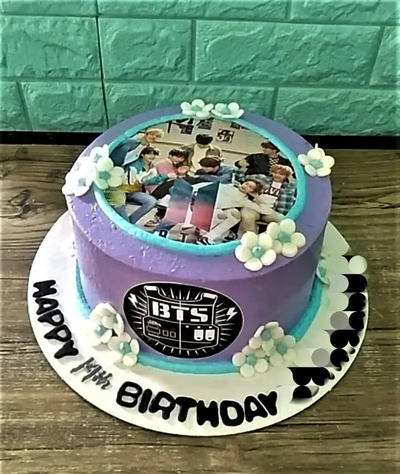 Purple BTS themed birthday cake with a group photo printout on top, white and teal fondant flowers, and a BTS logo on the side. Purple BTS themed birthday cake with a group photo printout on top, white and teal fondant flowers, and a BTS logo on the side.