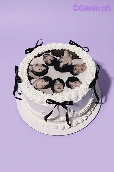 A white and black round 1-tier cake, BTS Kpop themed, with a printed group photo, white rosettes, and black ribbons. A white and black round 1-tier cake, BTS Kpop themed, with a printed group photo, white rosettes, and black ribbons.