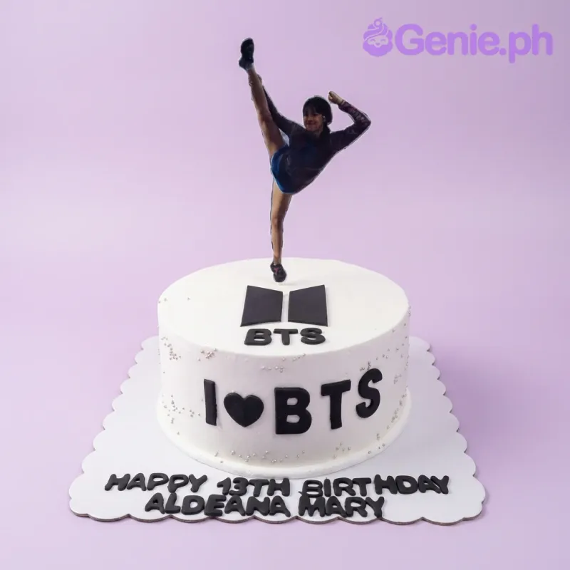 White BTS themed birthday cake with a gymnast printout topper and black fondant BTS logo and lettering. White BTS themed birthday cake with a gymnast printout topper and black fondant BTS logo and lettering.