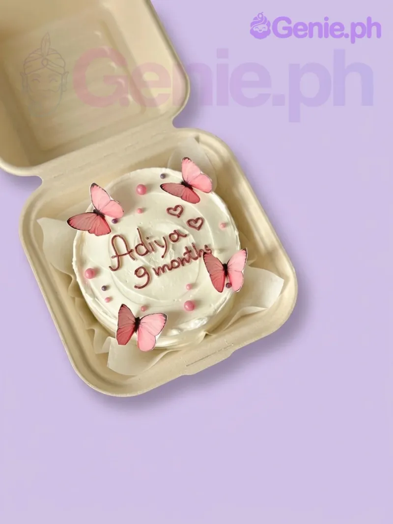 A white bento butterfly cake, featuring pink butterfly printouts, pink and purple sugar pearls, and an icing message. A white bento butterfly cake, featuring pink butterfly printouts, pink and purple sugar pearls, and an icing message.