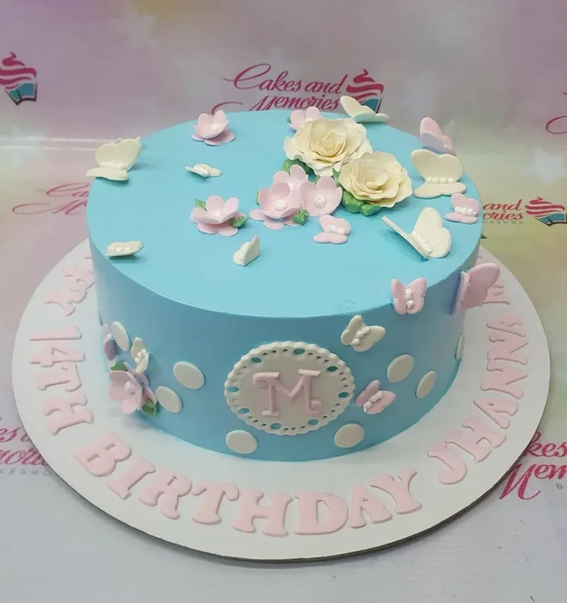 A pastel 1-Tier Butterfly Floral cake, featuring white roses, an 'M' monogram, butterflies, flowers, and a birthday message. A pastel 1-Tier Butterfly Floral cake, featuring white roses, an 'M' monogram, butterflies, flowers, and a birthday message.