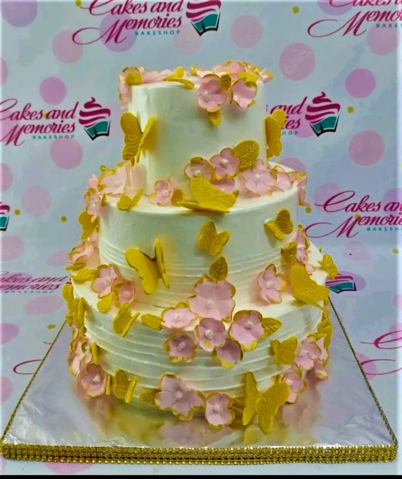 Elegant three-tier white cake decorated with pink gumpaste flowers and yellow butterflies. Elegant three-tier white cake decorated with pink gumpaste flowers and yellow butterflies.