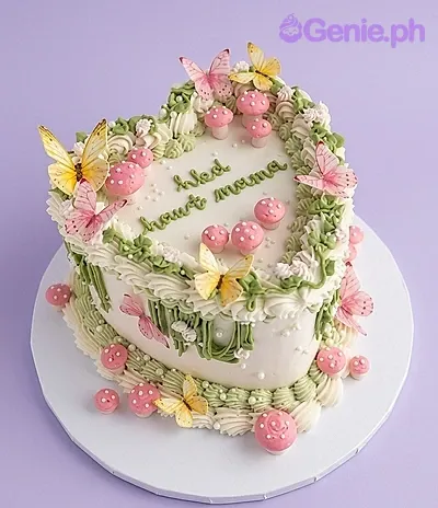 A white heart-shaped cake themed Butterfly Garden, featuring pink and yellow butterflies, pink mushrooms, and green piped vines. A white heart-shaped cake themed Butterfly Garden, featuring pink and yellow butterflies, pink mushrooms, and green piped vines.