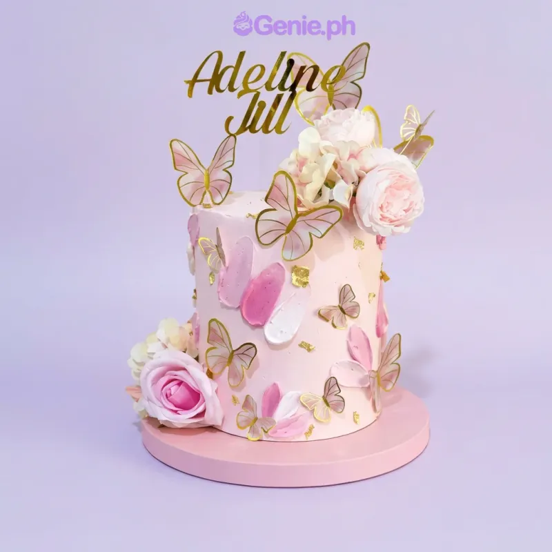 A pink 1-tier cake themed Butterfly Pink, with a gold name topper, pink roses, and gold butterfly decorations. A pink 1-tier cake themed Butterfly Pink, with a gold name topper, pink roses, and gold butterfly decorations.
