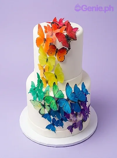 White 2-tier cake covered in colorful rainbow butterfly printouts White 2-tier cake covered in colorful rainbow butterfly printouts