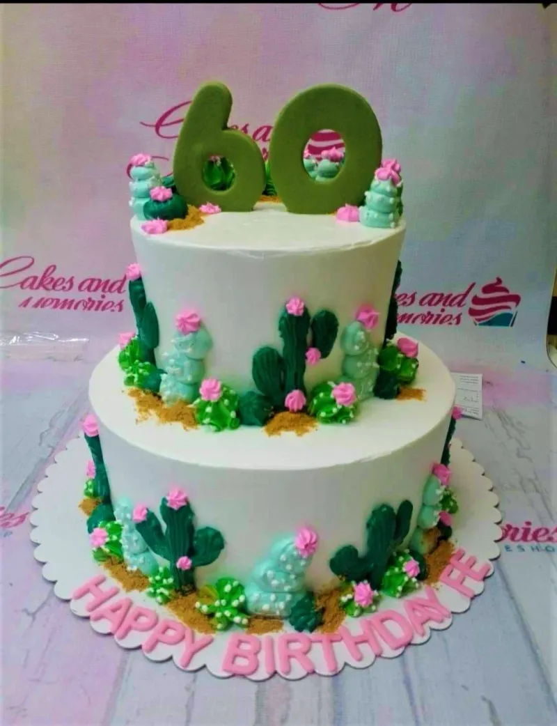 A white two-tier cake themed around Cactus, featuring a green number 60 topper, green piped cacti, and pink icing rosettes. A white two-tier cake themed around Cactus, featuring a green number 60 topper, green piped cacti, and pink icing rosettes.