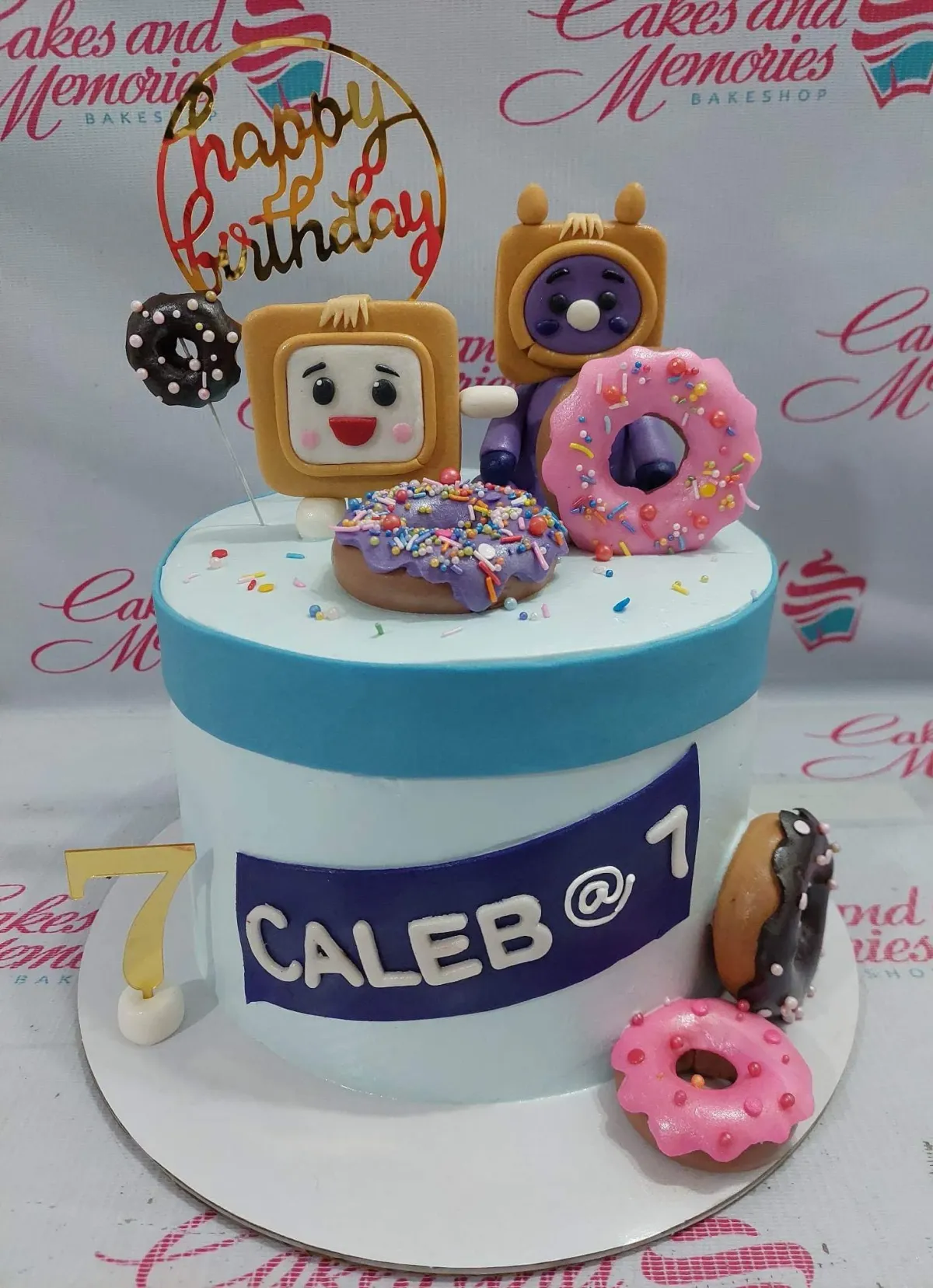 Light blue 1-tier birthday cake featuring edible 3D character figures, colorful donuts, and a gold Happy Birthday topper. Light blue 1-tier birthday cake featuring edible 3D character figures, colorful donuts, and a gold Happy Birthday topper.