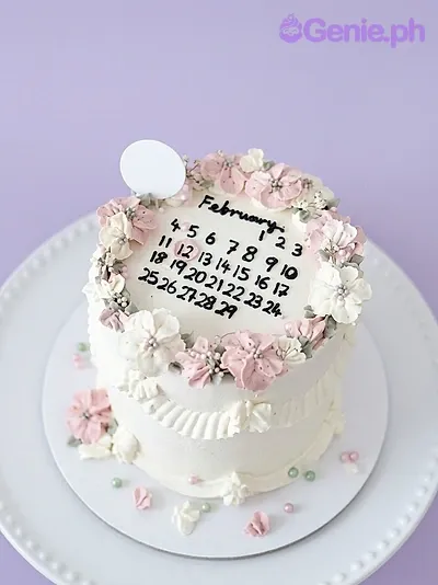 A white 1-tier cake themed around Calendar Floral, featuring a February calendar design, pink and white icing flowers, and silver beads. A white 1-tier cake themed around Calendar Floral, featuring a February calendar design, pink and white icing flowers, and silver beads.