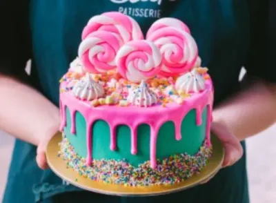 Teal cake with bright pink drip, rainbow sprinkles, and large pink and white swirl meringue pops on top. Teal cake with bright pink drip, rainbow sprinkles, and large pink and white swirl meringue pops on top.