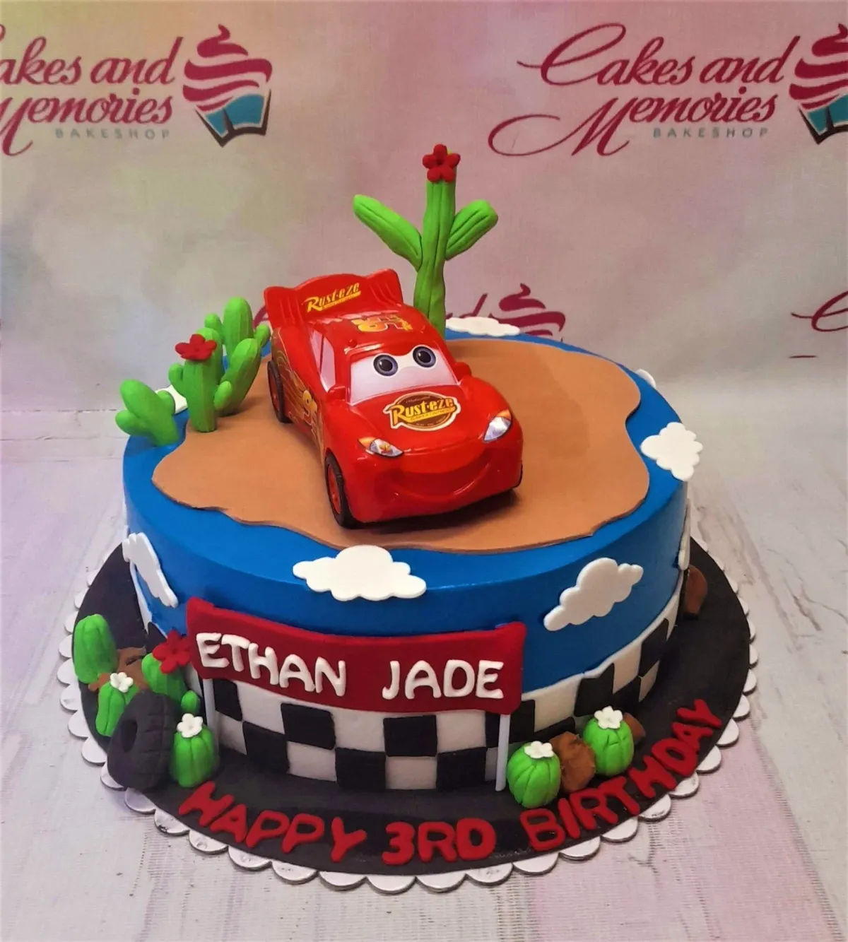 Disney Cars Lightning McQueen themed birthday cake with desert landscape, cactus toppers, and checkered flag design. Disney Cars Lightning McQueen themed birthday cake with desert landscape, cactus toppers, and checkered flag design.