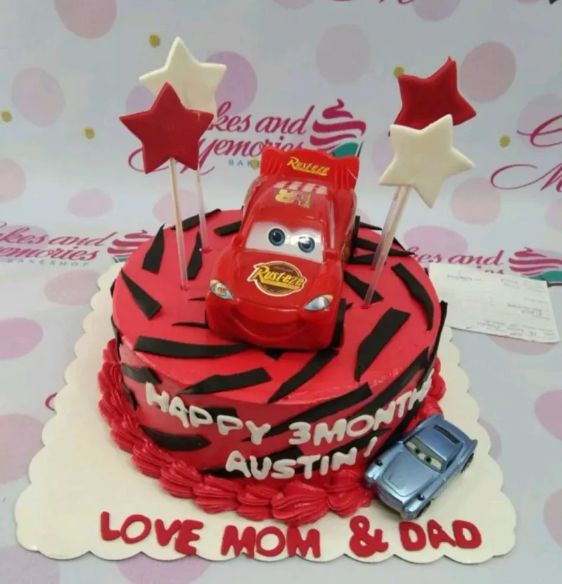 Red and black Lightning McQueen themed cake with toy cars and star toppers for a 3-month celebration. Red and black Lightning McQueen themed cake with toy cars and star toppers for a 3-month celebration.