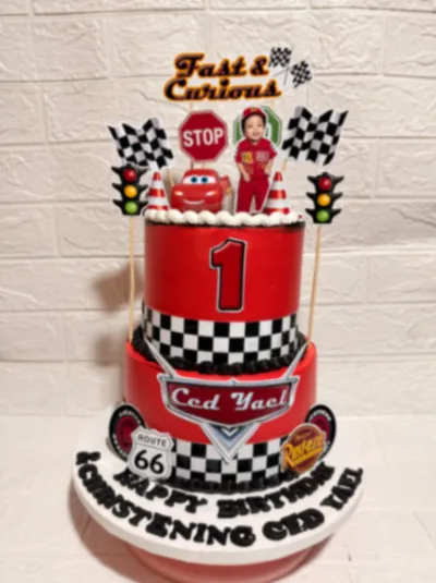 Red 2-tier fondant racing cake with checkered borders, Lightning McQueen toy, and racing printouts Red 2-tier fondant racing cake with checkered borders, Lightning McQueen toy, and racing printouts