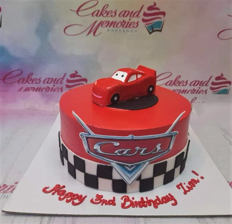 Red Disney Cars themed birthday cake with a 3D Lightning McQueen topper and checkered flag pattern on the side. Red Disney Cars themed birthday cake with a 3D Lightning McQueen topper and checkered flag pattern on the side.