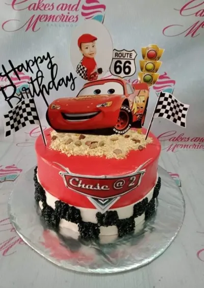 Red and white Disney Cars themed birthday cake with Lightning McQueen topper and checkered flag accents. Red and white Disney Cars themed birthday cake with Lightning McQueen topper and checkered flag accents.