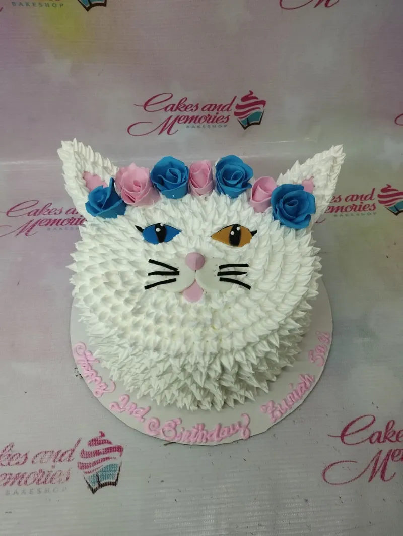 White cat-shaped cake with white icing fur texture, blue and pink fondant roses, and heterochromatic blue and orange eyes. White cat-shaped cake with white icing fur texture, blue and pink fondant roses, and heterochromatic blue and orange eyes.